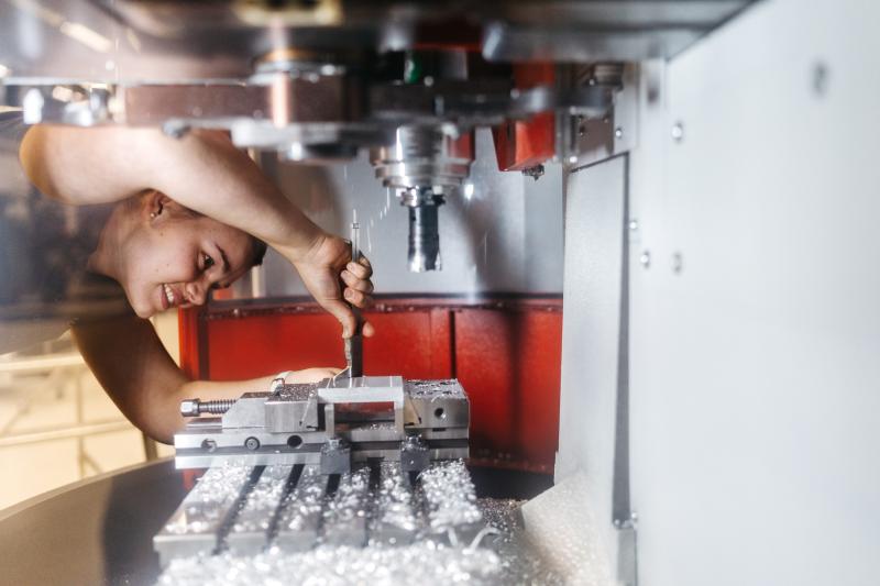 En tjej böjer sin fram och arbetar med ett verktyg i en industrimaskin